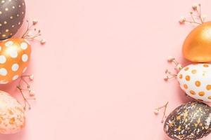 Top view of wooden painted eggs in gold, black and rose colors with branch of gypsophila on pink background. Happy easter background with copy space photo