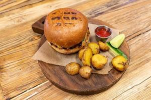 hamburguesa con carne servida con pepinos, cetchup y patata frita en tabla de cortar redonda. cena poco saludable foto