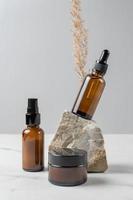 conjunto de productos cosméticos para el cuidado de la piel. concepto de presentación de embalaje sin marca. suero facial, lituina, crema facial en botellas de vidrio ámbar con piedras naturales y hierba de caña de pampa seca. foto