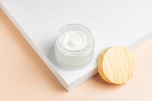 Cosmetic cream or moustirizer frosted glass open jar onwhite podium background. Open round glass jar with aesthetic swirls cream. Top view flatlay. Copy space photo