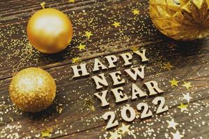 Happy new year 2022 text on wooden background surrounded golden christmas toys and fur tree branch. Festive greeting catd for holidays photo