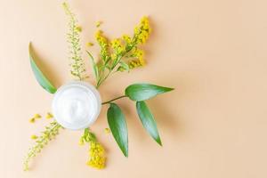 tarro de crema abierto para el cuidado de la piel con hojas verdes y flores sobre fondo beige. foto minimalista de primer plano para la presentación del producto de primavera