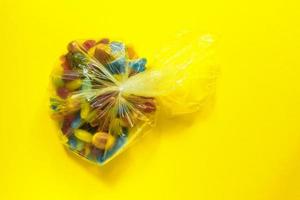 caramelos de gominolas glaseadas multicolores en envases de plástico sobre fondo de papel amarillo foto
