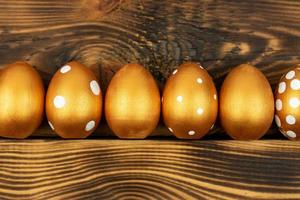 fondo festivo de pascua. vista superior de los huevos de pascua coloreados con pintura dorada sobre fondo de madera oscura. varios diseños punteados foto