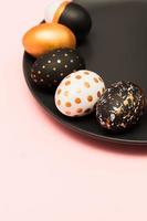 Pink background with white, black and golden decorated eggs on black plate. Trendy easter flat lay with copy space. photo