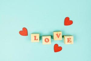 Red hearts and wooden cubes with text LOVE on blue background. Creative flat lay with copy space. Festive greeting card for St Valentines day. photo