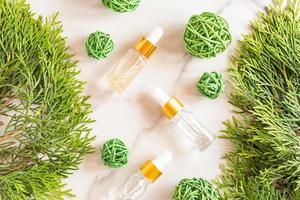 Glass dropper bottles with cosmetic oil, essential or serum on marble background with thuja branches and ratang balls. Concept of natural organic cosmetics. Herbal homeopathic products. photo