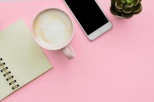 feminini desk workspace with smartphone, blank notepad, cactus, cup of coffee on pink background. flat lay, top view photo