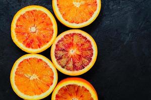 Sliced Sicilian blood oranges on black stone natural background, top view. photo