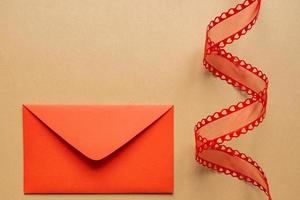 Valentine's day or Wedding romantic concept. Twisted decorative ribbon and red envelope with red hearts on beige background. photo