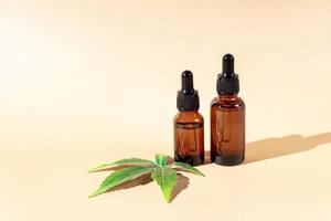 Glass dropper bottles with cbd oil on beige background with marijuana leaf. Hemp based cosmetics. Natural herbal hemp essential oil in a glass pipette bottle. photo