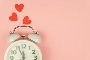 Pink Background with white alarm clock and red hearts. Creative layout. Top view. Time for love and greetings. photo