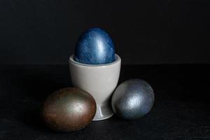 Dark blue Easter egg in ceramic holder on black background. Concept of minimal festive Easter backdrop photo