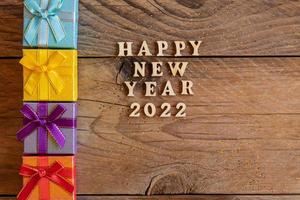 Multicolored gift boxs. New year presents on wooden table. Tex Happy new year 2022. Festive greeting card. Flat lay. photo