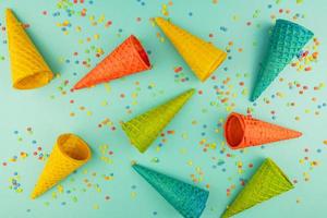 bright multicolored ice-cream waffle cones on blue background with scattered confetti sugar sprinkles. photo