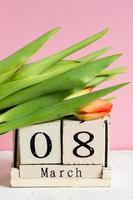 día internacional de la mujer. calendario de madera 8 de marzo y tulipanes rojos sobre fondo rosa foto