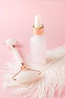 Home treatment concept. Skin care products and tools. Face serum and quartz roller on pink background photo