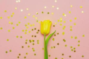 Creative festive backgound with single yellow tulip and golden star confetti. photo