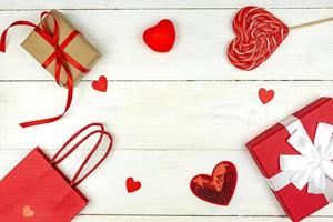 Creative Valentine Day romantic composition with red hearts, satin ribbon, lollipop, gift box and paper bag on white background. Mockup with copy space for blogs and social media. photo