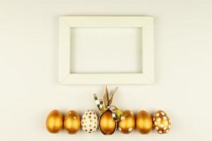 Easter festive decoration. Top view of easter eggs colored with golden paint and empty mock-up photo frame. Various dotted designs. White background.