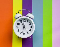 white alarm clock on multicolored striped background with copy space for text. photo