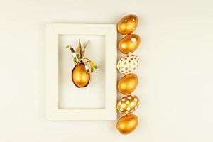 Easter festive decoration. Top view of easter eggs colored with golden paint and empty mock-up photo frame. Various dotted designs. White background.