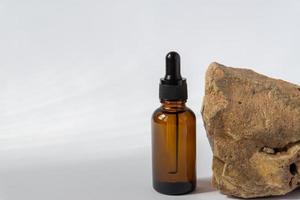 Dark glass cosmetic bottle with a dropper on a grey background with stone. Natural cosmetics concept, natural essential oil and skin care products photo