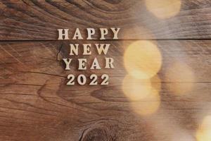 Happy New Year 2022. Symbol made from wooden letters and numbers 2022 on wooden background with golden bokeh photo