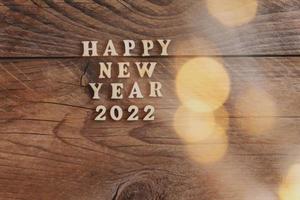 feliz año nuevo 2022. símbolo hecho de letras de madera y números 2022 sobre fondo de madera con bokeh dorado foto