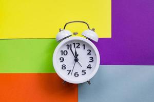 white alarm clock on abstract multicolored paper background. Minimal flat lay. photo