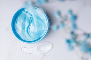 Eye patches in a plastic container, top view. Hydrogel patches with peptides for the area around the eyes. Blue gel patches with a plastic spatula in a jar on a marble background. photo