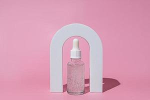 Beauty collagen face oil in a glass dropper bottle in Arch on pink background. Trendy shoot of cosmetics packaging. Essential oil with natural ingredients. Cruelty free cosmetics photo