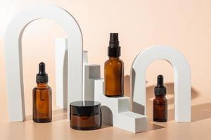 Amber glass dropper bottles and cream jar on white podiums. Beige background. Container mockup with cosmetic oil or serum. Showcase for the presentation skincare products. photo