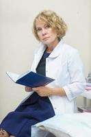 middle aged woman in white coat holding blue daily planner. Doctor female, medical professional photo
