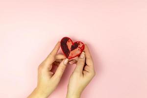 Female hands holding red sequin heart on pink background. Creative minimal layout with copy space photo