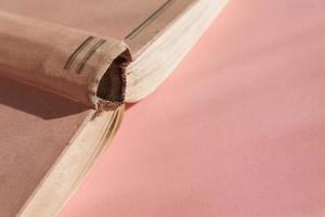 Open hardcover old book on pink background with copy space. Educational concept photo