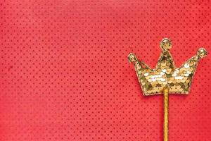 golden magic stick from sequins in crown shape on red background. Creative flat lay in minimal style. Copy space for text photo