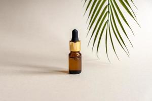 A glass cosmetic bottle with a dropper on a grey background with palm leaves. Natural cosmetics concept, natural essential oil photo