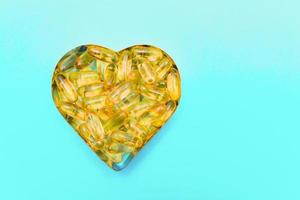 Fish oil capsules in a heart shape plate on blue background, vitamin D supplement, top view with copy space photo