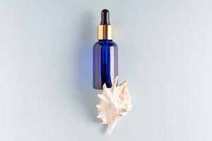 Serum bottle with pipette on blue background. Top view, flat lay. Dermatology science cosmetic laboratory. Natural medicine cosmetic research, organic skin care products with sea minerals and collagen photo