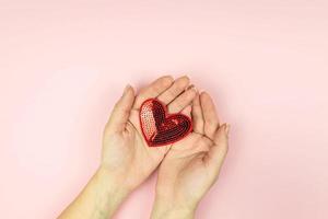 Female hands holding red sequin heart on pink background. Creative minimal layout with copy space photo