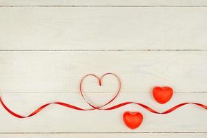 Creative Valentine Day romantic composition with red hearts, satin ribbon on wooden background. Mockup with copy space for blogs and social media. photo