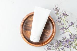 White cosmetic cream tube, balm jar mockup in wooden bowl on white marble background. Make up product blank container. Body and face care photo