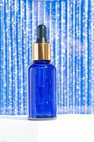 Pipette dropper bottle with beauty face oil on a sparkling blue background. Face and body treatment gift concept. photo