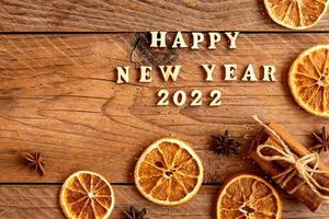 Cinnamon sticks, slices of dried orange, star anise and quote happy new year 2022 on wooden background with copy space. Top view. Christmas and New Year celebration concept. photo