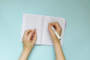 young woman makes notes in her planning or dairy on blue background. Planning concept. Flat lay style. photo