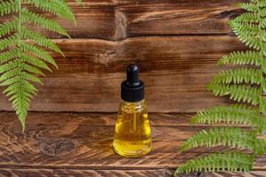 Skin care serum in dropper bottle on wooden board with fern leaves. SPA natural organic beauty product packaging design. photo