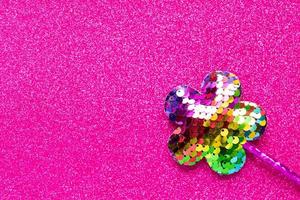 magic stick from sequins in flower shape on pink glitter background. Creative flat lay close up photo
