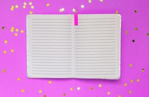 Open empty notebook on a pink background with stars confetti. Top view. Space for text or design photo