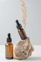 Anti aging serum with collagen and peptides in dark glass bottles with dropper on gray background with natural stone and dry pampas grass. Skincare essence for healthy skin. photo